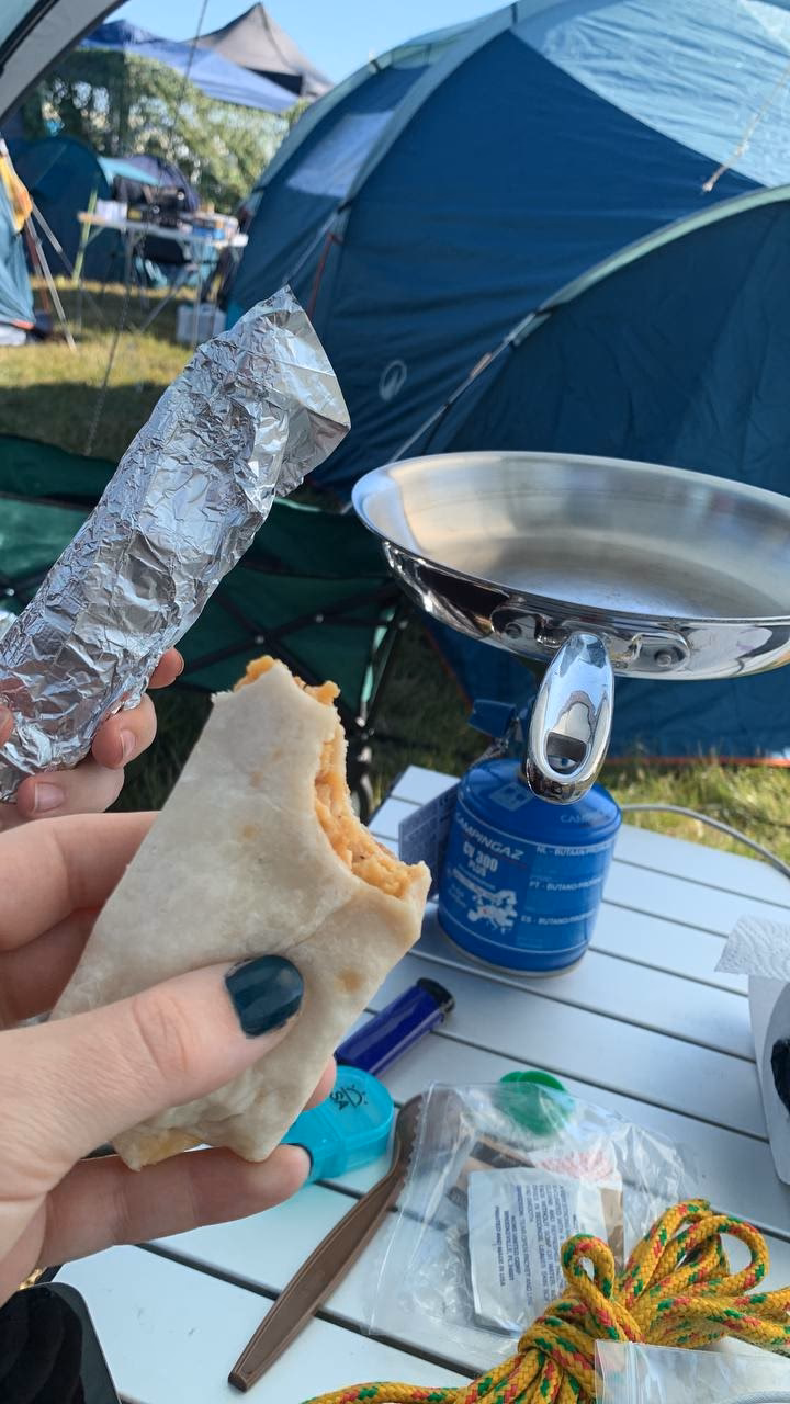 A thin breakfast burrito is held in front of a clean pan. Behind is a foil wrapped burrito.